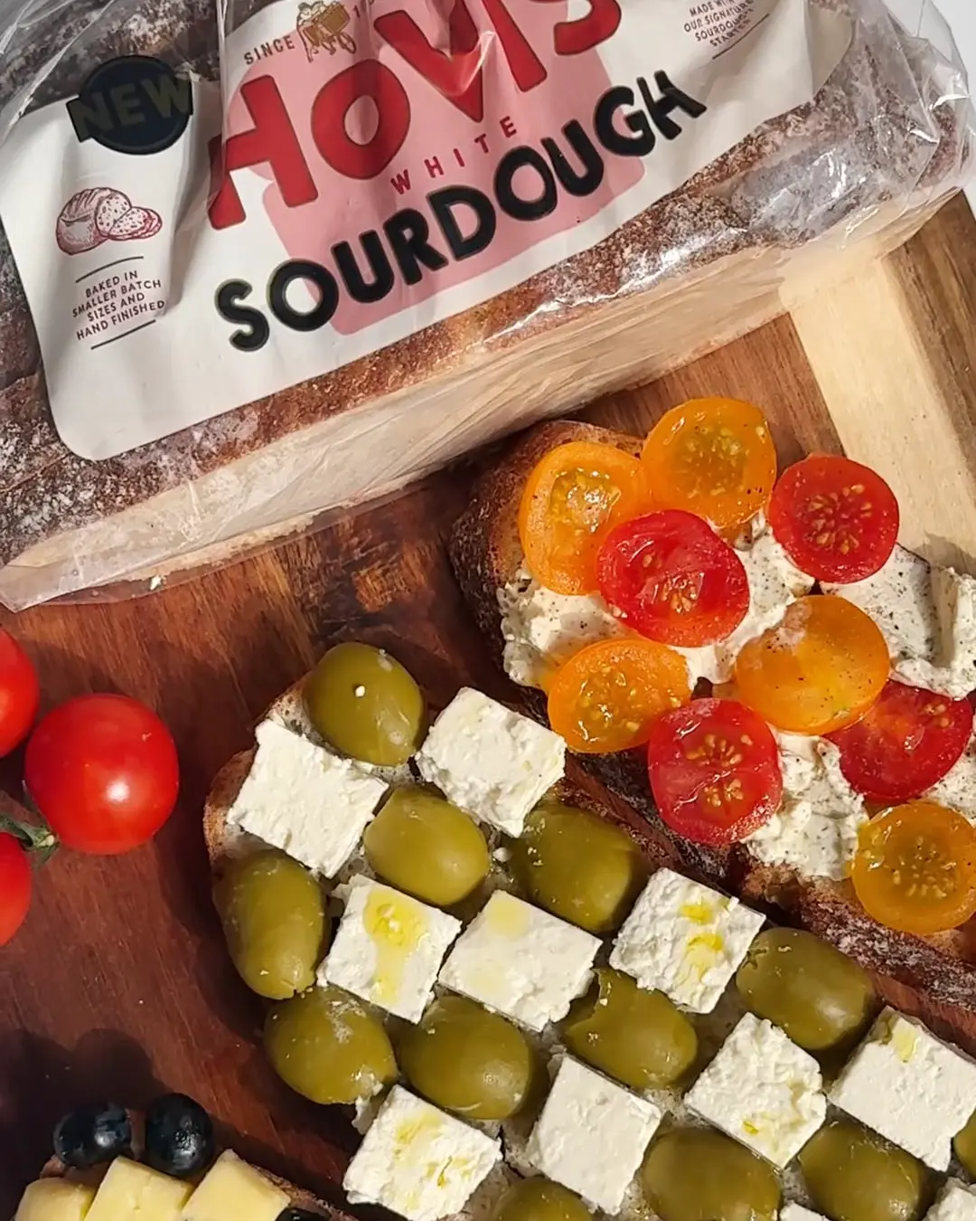 Two gourmet sourdough toasts, one with sliced tomatoes, the other with feta and green olives, next to Hovis White Sourdough.