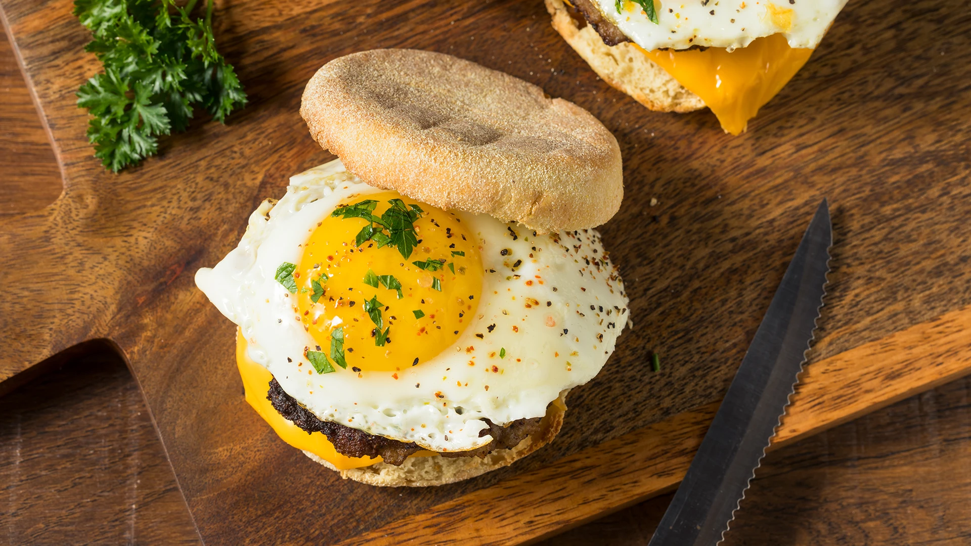 Hovis Soft White Muffins filled with molten cheese, a burger patty, and a fried egg, topped with ground black pepper and chopped greens.