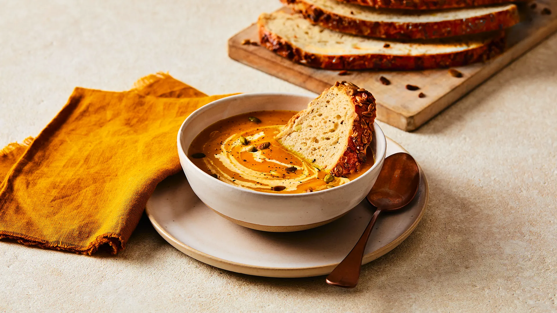 A close-up image of a Hovis®  Seeded Sourdough slice in a bowl of Butternut Squash Soup with extra Seeded Sourdough Slices in the background