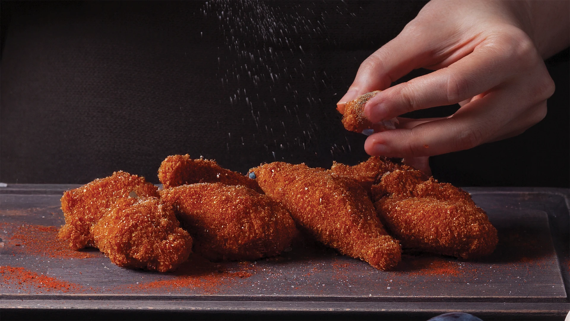Someone is spreading cajun spice on breaded chicken on a wooden chopping board