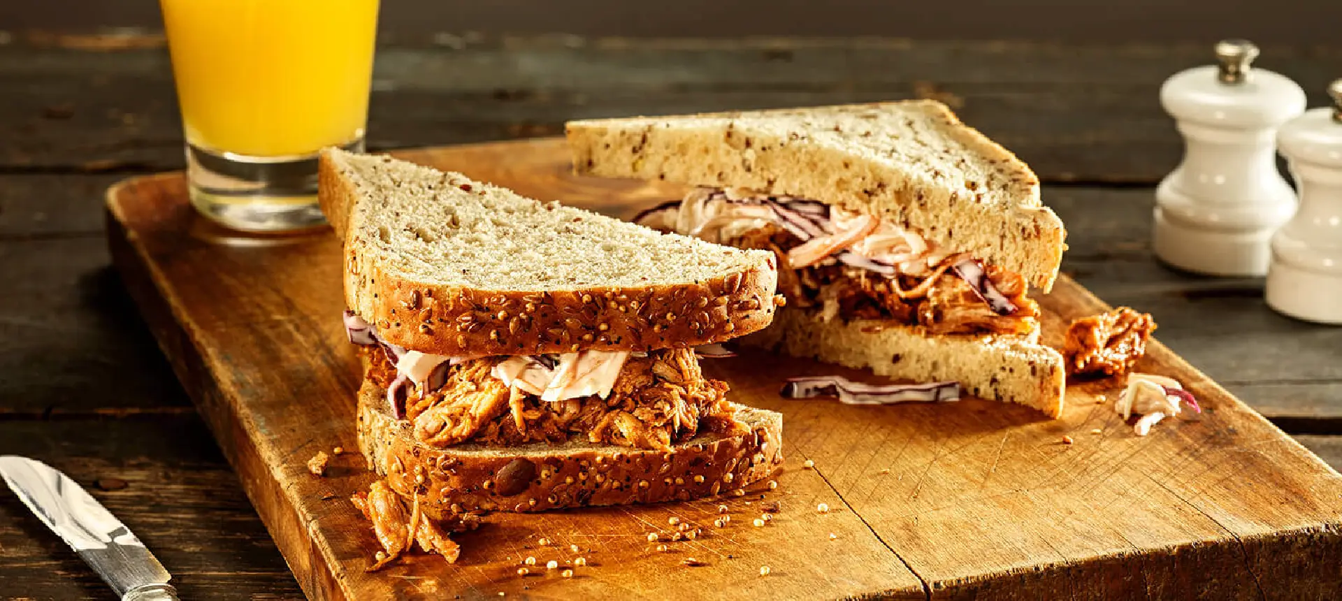 Two halves of a pulled pork sandwich made with Hovis Seed Sensations Original bread, filled with pulled pork and coleslaw, on a wooden chopping board.